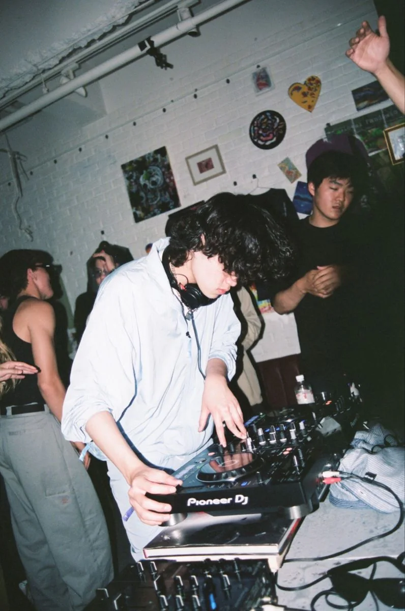 A DJ using decks surrounded by people in an intimate indoor space.