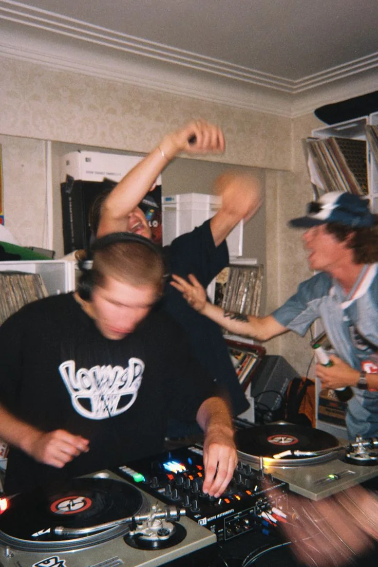 A DJ mixing vinyl records while people dance in a small room.